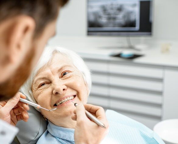 An elderly woman undergoes a dental examination with a male dentist, discussing fixed hybrids at Spencer Dental in Maryville