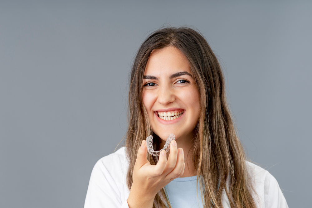 A beautiful smiling woman holding an Invisalign aligner, showcasing services at Spencer Dental in Maryville